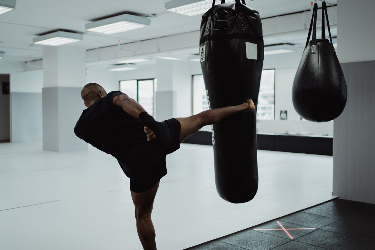 Athlete executing a high kick on punching bag in a gym setting. Dynamic fitness training.