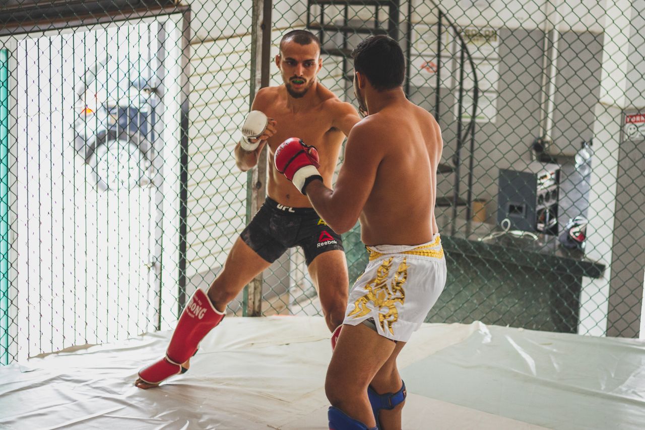 services-02 Two men engage in intense kickboxing sparring inside a gym arena.